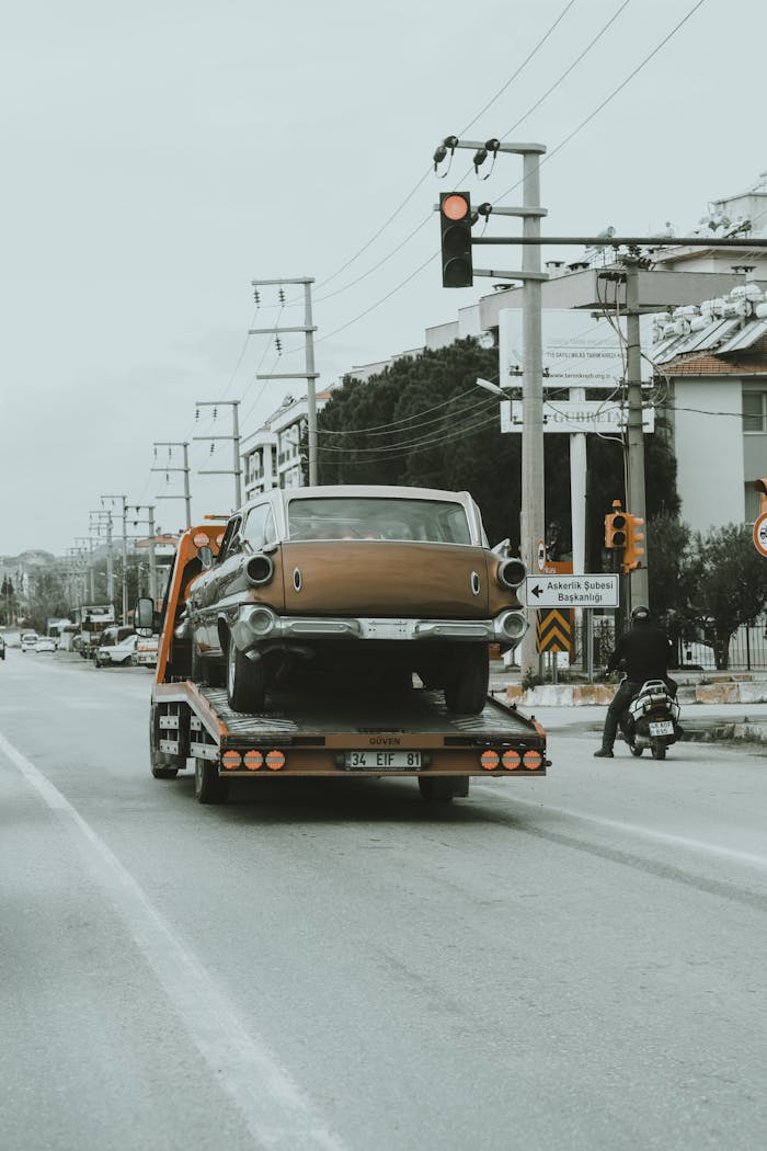 Crafting Captivating Headlines: Your awesome post title goes here A vintage car is being towed through city streets on a tow truck, showcasing an urban environment.